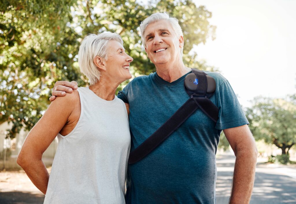 Older white couple in their 50s, man wearing OrthoCor One device on his shoulder.